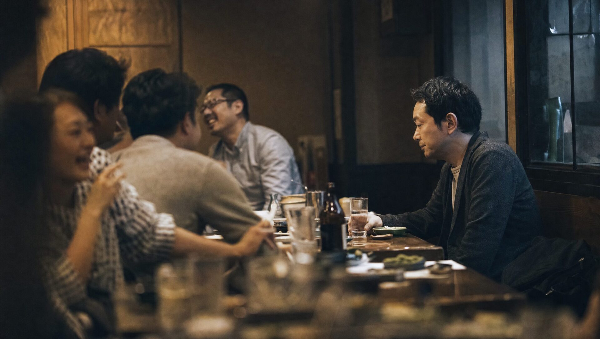 居酒屋で、会話している人たちの輪から少し離れて一人で座っている男性