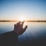 landscape photography of person's hand in front of sun